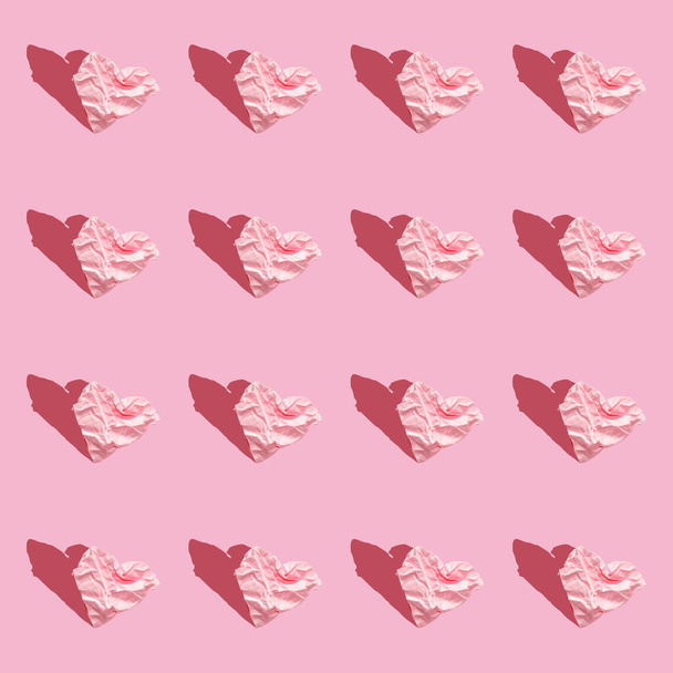 pattern - hearts from crumpled paper on pink background. Seamless background with hearts, hard light. Congratulatory creative pattern of paper hearts on pastel pink background with hard shadows. - Photo, image