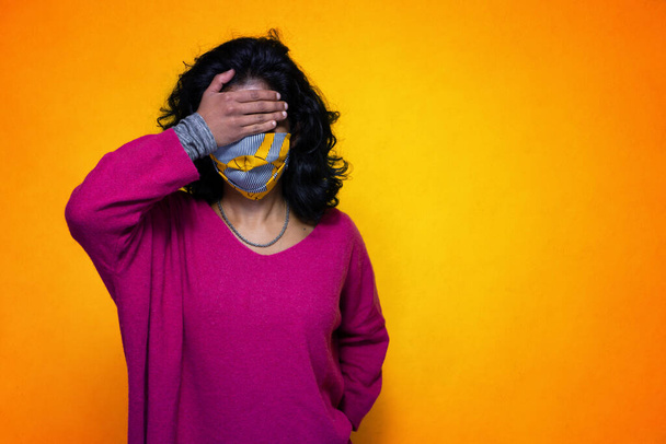 Beautiful young indian woman covers her eyes with her hand with covid 19 mask protection - Pretty Sri Lanka girl uses protection from pandemic covid 19 flue covering her face - Photo, Image