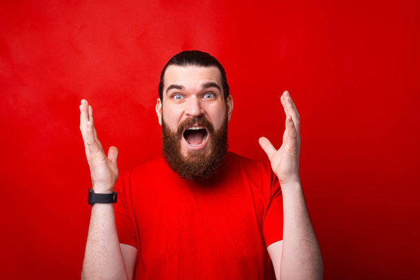 Wow, portré csodálkozó és meglepett fiatal szakállas férfi piros háttér - Fotó, kép