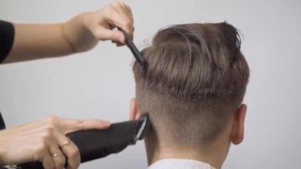 Meisje kapper knipt het haar van de jongen met een tondeuse op de slapen en de achterkant van het hoofd. - Video