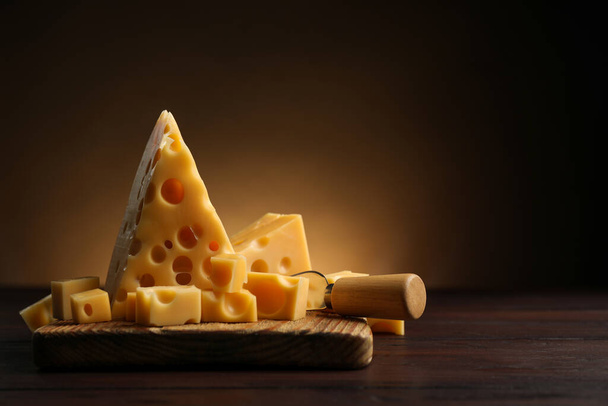 Pieces of delicious cheese and knife on wooden table. Space for text - Fotoğraf, Görsel