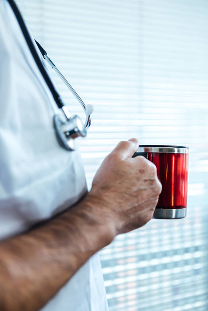 Dojrzały lekarz - pielęgniarka pijąca kawę w oknie szpitala. Covid-19 i koncepcja medycyny - Zdjęcie, obraz