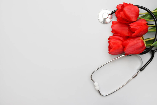 Bouquet de ps rouges et stéthoscope sur table blanche. Vue du dessus avec espace de copie. Journée nationale des médecins. Bonne journée infirmière. - Photo, image