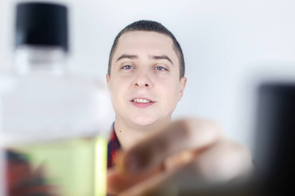 Close-up van een man in de badkamer met behulp van een mondwater. Tandheelkundige zorg concept. Procedure na tandenpoetsen. Antibacteriële mond vloeistof. Giet, spoelt en spuugt vloeistof uit. Kijk in de spiegel. - Foto, afbeelding
