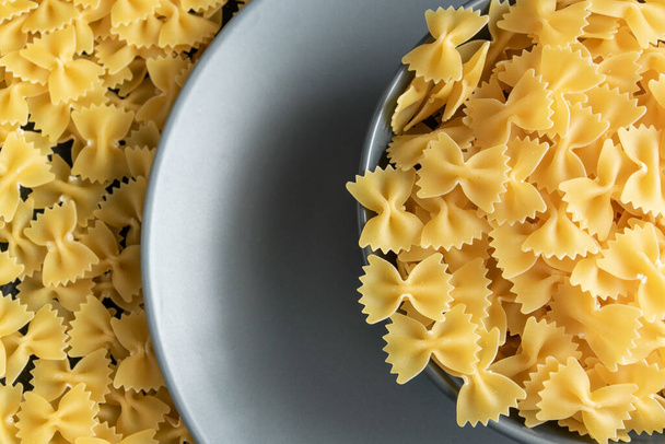 Food background - dry farfalle pasta on grey plate, whole wheat uncooked ingredient, space for text - Photo, Image