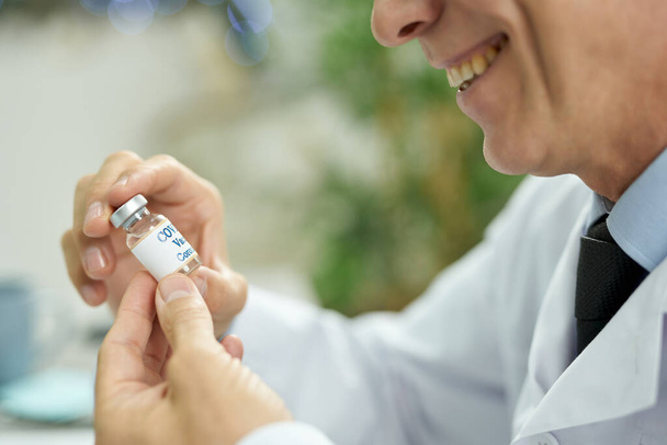 Cheerful doctor holding bottle of covid-19 vaccine - Zdjęcie, obraz