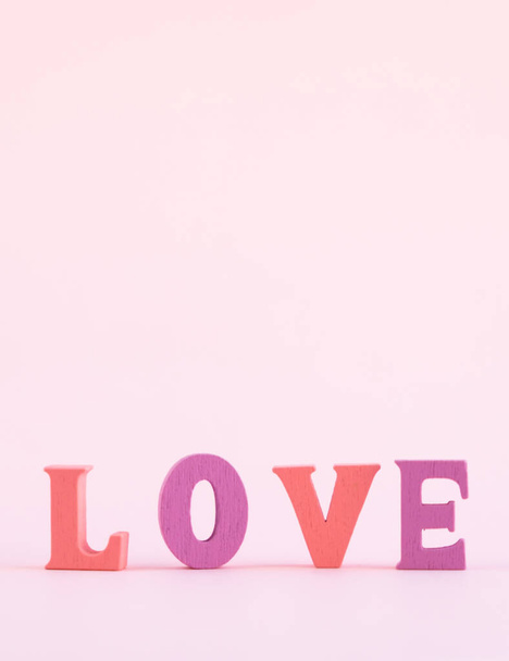 The word love in multicolored letters on a pastel pink background. Happy Valentine's Day, Happy Mother's Day, 8 March. Flat lay. Vertical photo. - Valokuva, kuva