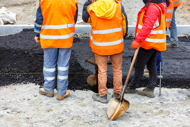 Um grupo de trabalho de trabalhadores rodoviários em macacão laranja se reuniu para discutir um plano de trabalho para pavimentar a seção da estrada com asfalto quente fresco. Espaço de cópia. - Foto, Imagem