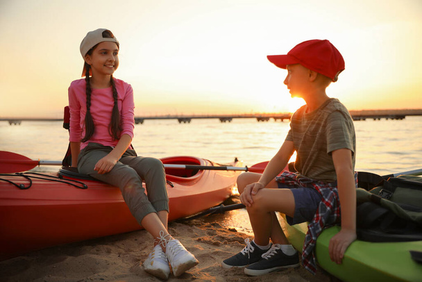 Happy children sitting on kayaks near river at sunset. Summer camp - Foto, immagini
