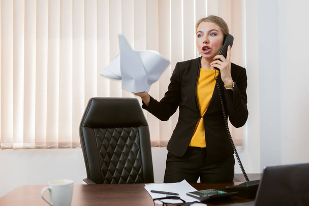 Злая эмоциональная женщина-босс разговаривает по телефону в своем офисе - Фото, изображение
