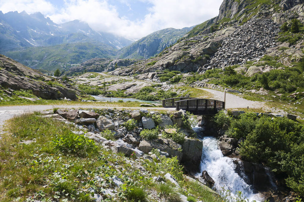 Holzbrücke, die den Fluss überquert und schöne Aussicht auf die Berge vom Weg zu den Seen von Cornisello im Val Nambrone im Trentino, Reisen und Landschaften in Italien  - Foto, Bild