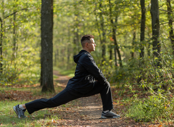Активный спортсмен тренирует разминку или растяжку в осеннем лесу. Здоровый образ жизни. Занятия на открытом воздухе - Фото, изображение