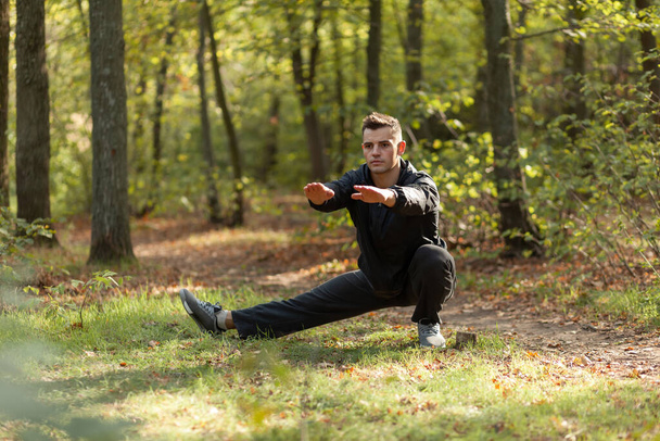 Активный спортсмен тренирует разминку в осеннем лесу. Здоровый образ жизни. Занятия на открытом воздухе - Фото, изображение