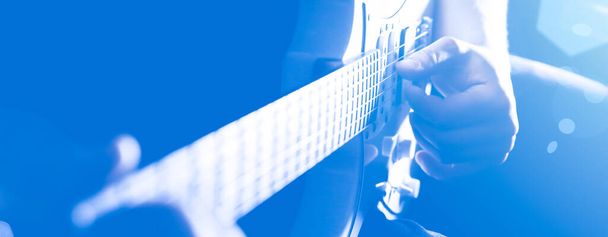 Soft focus photo. Man playing electric guitar in the shadow. Musical instrument photo. Musician under the spotlight. Creative style with light shadows. - 写真・画像
