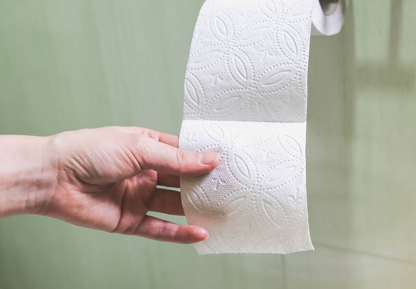 Μια γυναίκα κρατάει χαρτί τουαλέτας στο χέρι της.. - Φωτογραφία, εικόνα