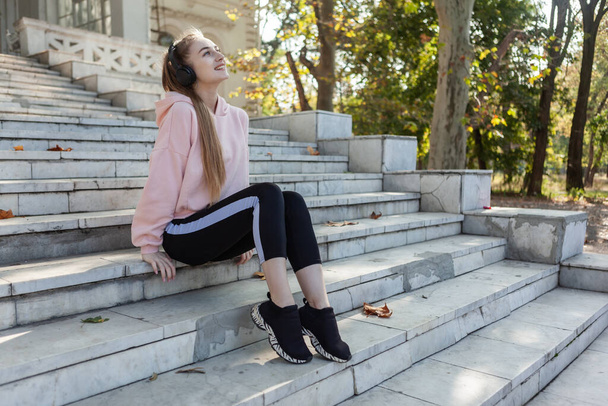 Стройная привлекательная женщина сидит на ступеньках и делает селфи на смартфоне на улице - Фото, изображение