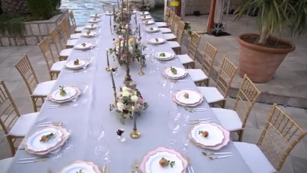 Stół na bankiecie weselnym, ozdobiony kwiatami, świeczniki z płonącymi świecami i młode granaty na molo nad morzem - Materiał filmowy, wideo