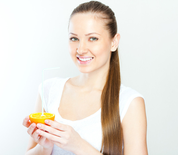 Attractive smiling young woman drinking orange juice straight from fruit - Foto, imagen