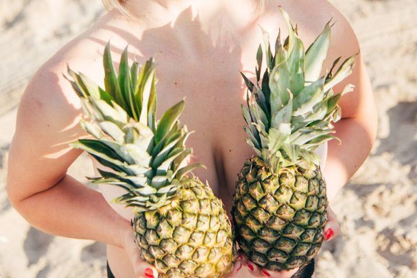 Two pineapples in female hands on the background of a female body - Foto, immagini