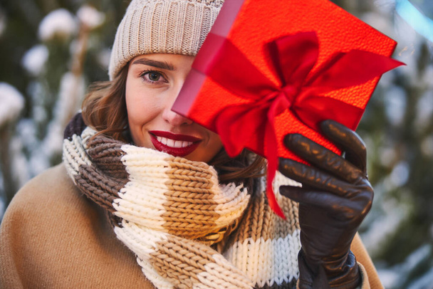 Smiling beautiful woman holding Christmas present outdoors - Foto, afbeelding