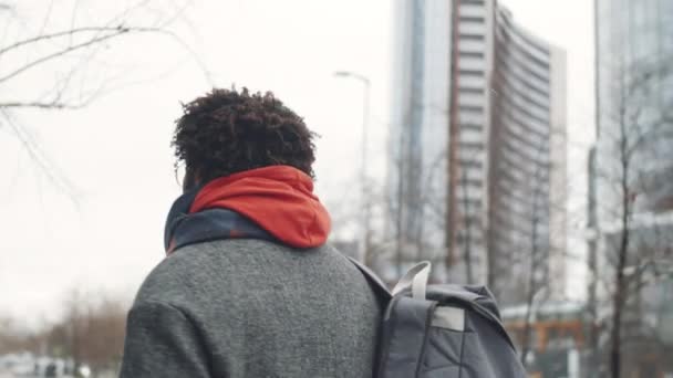 Egy fiatal afro-amerikai férfi nyomában, aki kávéért iszik, és télen a városban sétál. - Felvétel, videó