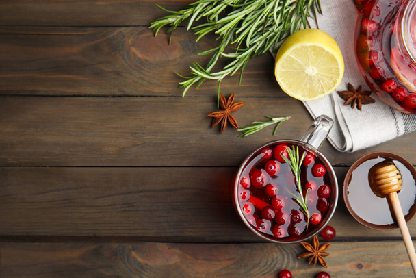 Tasty hot cranberry tea and fresh ingredients on wooden table, flat lay. Space for text - Zdjęcie, obraz