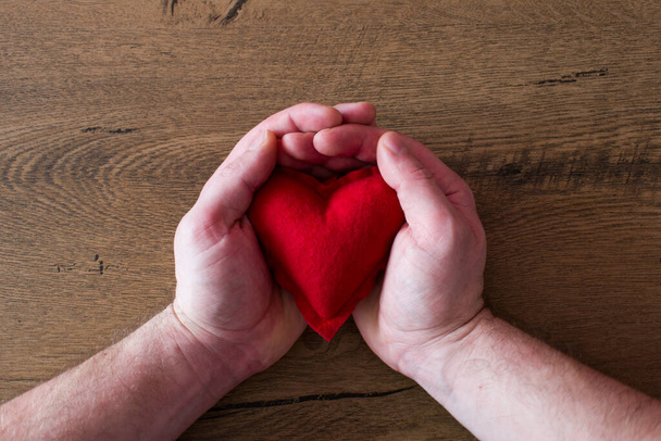 Corazón rojo en mans manos sobre fondo de madera - Foto, Imagen