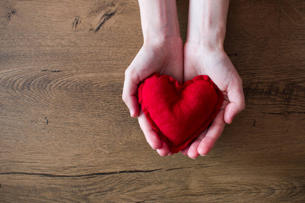 Weibliche Hände mit rotem Herz auf hölzernem Hintergrund. Valentinstag Grußkarte Konzept - Foto, Bild