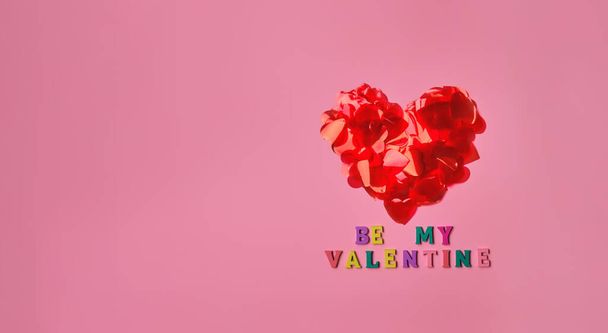 Be My Valentine kirjoitus merkintä Ystävänpäivä onnittelukortti. Punainen sydän on valmistettu terälehtien muotoinen sydämet, vaaleanpunainen tausta kirjoitus monivärinen puinen kirjaimia. Lippu Kopioi tilaa - Valokuva, kuva