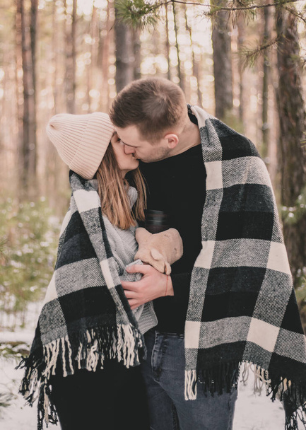 Muž objímá a líbá ženu zakrytou přikrývkou na pozadí zimního borového lesa - Fotografie, Obrázek