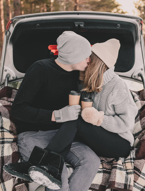 Couple sitting on a blanket in the trunk of a car and kissing on the background of a pine forest - Foto, imagen