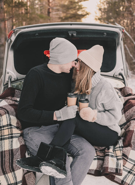Bir arabanın bagajında battaniyeye oturmuş çam ormanının arka planında öpüşen çift. - Fotoğraf, Görsel