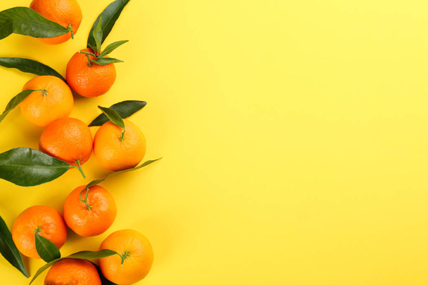 Fresh tangerines with green leaves on yellow background, flat lay. Space for text - Photo, image
