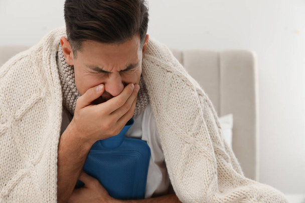 Ill man with hot water bottle coughing at home - Photo, Image