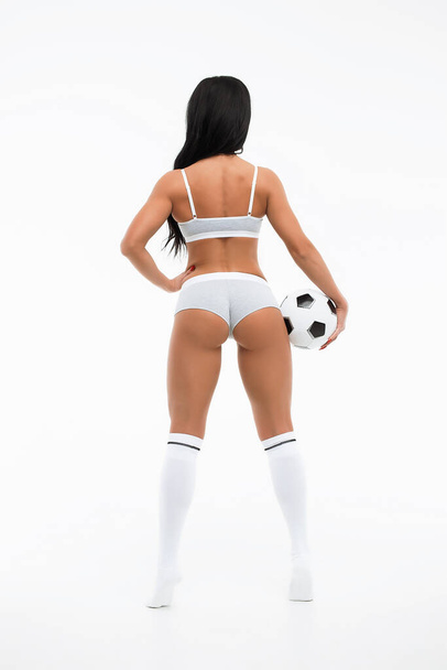 Sporty satisfied brunette in white underwear and knee socks with whistle on neck and football in hand isolated on white background - Foto, imagen