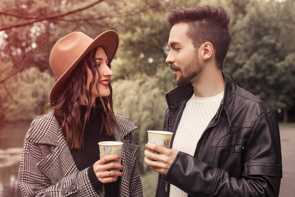 Portrait of heterosexual couple standing outside in the city park in cloudy rainy moody weather, spending time together, have fun, speaking and drinking hot tea. Romantic dating in botanical garden. - Fotografie, Obrázek