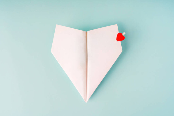 Een papieren vliegtuig met een hartvormige wasknijper op een blauwe achtergrond. Het concept van een liefdesboodschap. Valentijnsdag, liefdesbriefje - Foto, afbeelding