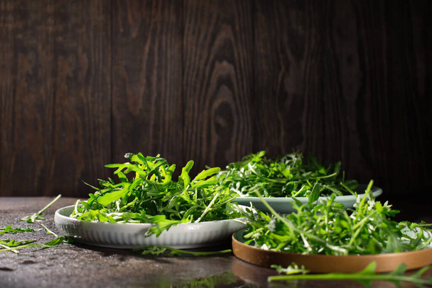 Fresh green raw leaves of arugula rucola salad on dark rustic wooden background. Selective focus, copy space. Fresh healthy food, diet concept.  - Fotó, kép