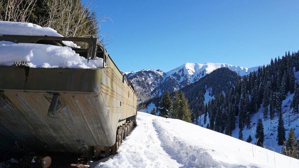Elhagyott katonai járművek a havas hegyekben. Retro off-road gépek katonai évei. Gépezet a hegyekben és az erdőben. Kék ég és árnyékok. Egy elhagyatott tank egy domb tetején.. - Fotó, kép