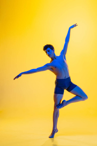 Young and graceful ballet dancer isolated on yellow studio background in neon light. Art, motion, action, flexibility, inspiration concept. - Фото, зображення