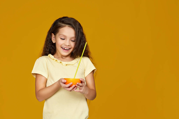 child girl holding fresh juicy grapefruit and drinks juice - 写真・画像