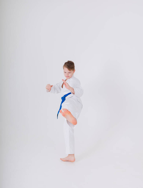 teenager boy in a white kimono makes a kick on a white background with a place for text. Hand-to-hand combat for children - Photo, Image