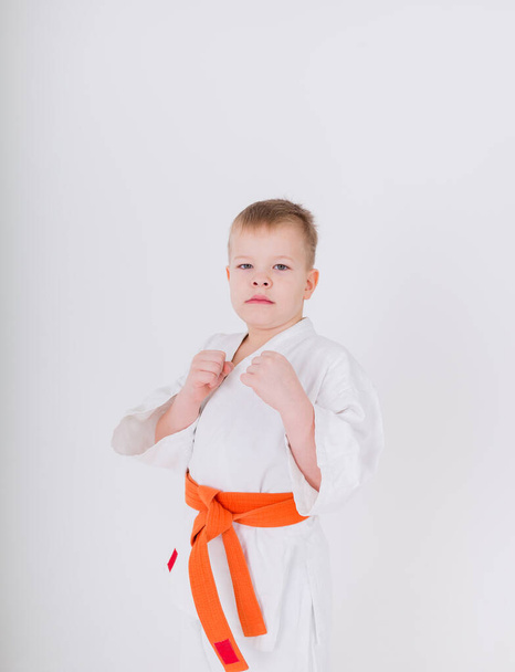 portret van een kleine jongen in een witte kimono met een oranje gordel die in een pose op een witte achtergrond staat met ruimte voor tekst - Foto, afbeelding