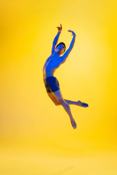 Young and graceful ballet dancer isolated on yellow studio background in neon light. Art, motion, action, flexibility, inspiration concept. - Fotoğraf, Görsel