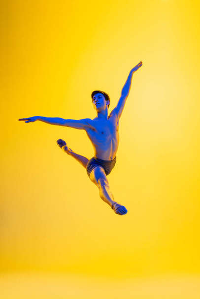 Young and graceful ballet dancer isolated on yellow studio background in neon light. Art, motion, action, flexibility, inspiration concept. - Fotó, kép