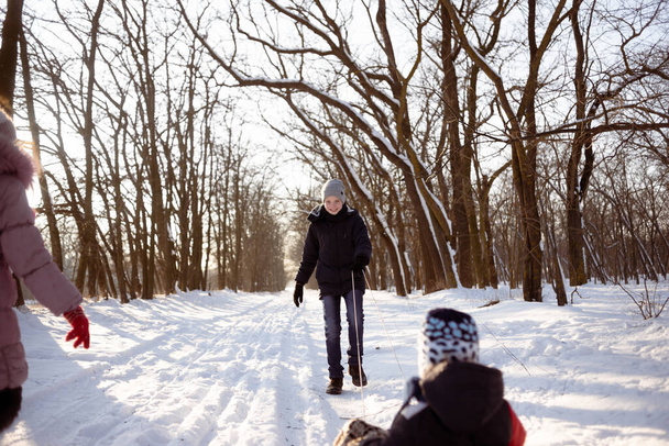 Der Junge ist mit seinem jüngeren Bruder auf einem Schlitten auf einer verschneiten Straße im Wald unterwegs. Kinder ruhen im Winter. - Foto, Bild