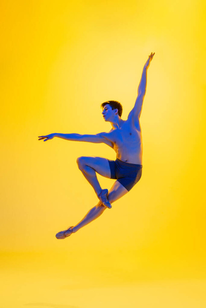 Young and graceful ballet dancer isolated on yellow studio background in neon light. Art, motion, action, flexibility, inspiration concept. - Foto, Imagen