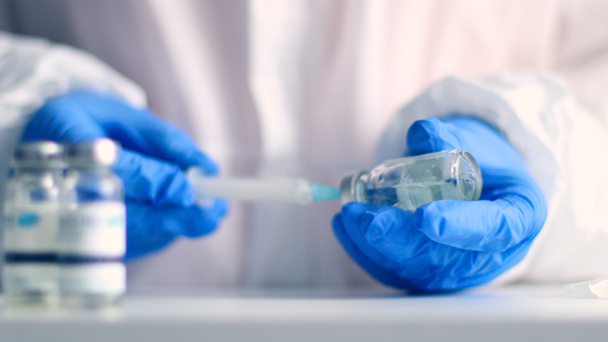 青いラテックス手袋の医師は、コロナウイルス、インフルエンザ、はしか病に対する医療研究所で高齢者の注射のためのガラス瓶から薬で注射器で埋めます - 写真・画像