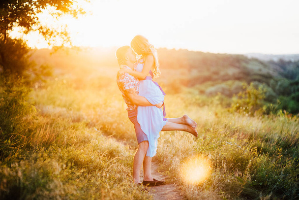blonde girl with loose hair in a light blue dress and a guy in the light of sunset in nature - Photo, Image