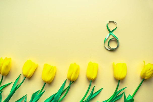 Slunečné květinové aranžmá. Žluté čerstvé tulipány s číslem 8 uprostřed na žlutém papírovém pozadí. Pozdrav na Mezinárodní den žen 8. března. Selektivní soustředění. Ležel. Kopírovat prostor. - Fotografie, Obrázek
